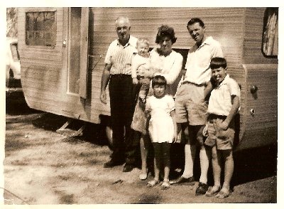 1968. Dad and Mum with a hired Millard caravan with my Grandfather on holidays.Iam in my mums arms and my sister and brother are in front.My eldest sister is taking the photo.